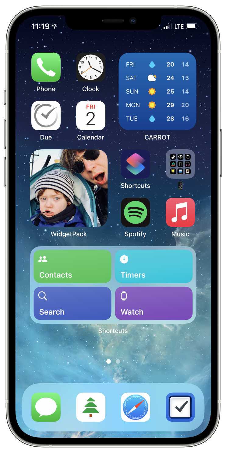 An iPhone showing a home screen. The background is blue with stars in the upper quadrant and a nebula in the lower quadrant. The layout is described in the next section. The widget in the middle-right shows a picture of a small child with a winter hat and an adult male wearing sun glasses showing an expression of mock surprise.